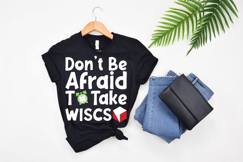 May include: Black t-shirt with white text that reads "Don't Be Afraid To Take WISC-S". A green alarm clock and a red cube are next to the text.