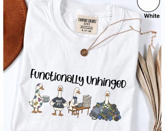 Może przedstawiać: Biały t-shirt z napisem "Functionally Unhinged" nad grafiką przedstawiającą cztery gęsi. Jedna gęś trzyma pojemnik z masą, jedna ma na sobie koszulkę "NOT PT", jedna siedzi przy biurku z laptopem i papierami, a jedna siedzi w stosie włóczki.