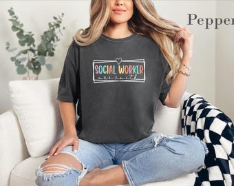 Könnte beinhalten: Ein anthrazitfarbenes Kurzarm-T-Shirt mit einem weißen rechteckigen Rahmen und einem kleinen Herz darüber. Im Inneren steht der Text SOCIAL WORKER in bunten Buchstaben, darunter der Name mrs smith in weißer Schreibschrift.