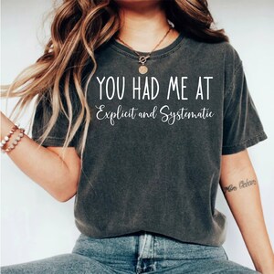 May include: A dark gray t-shirt with the text "You had me at Explicit and Systematic" printed in white.