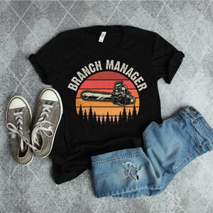 May include: Black t-shirt with a vintage-style graphic of a chainsaw and the text "Branch Manager".