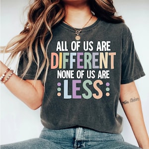 May include: A dark grey t-shirt with the text "All of us are different, none of us are :less:" in colorful letters.