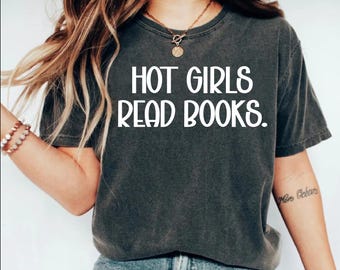 May include: Dark gray t-shirt with the text "HOT GIRLS READ BOOKS" in white block letters. The shirt is a crew neck style and appears to be made of a soft, comfortable material. The overall aesthetic is casual and relaxed.