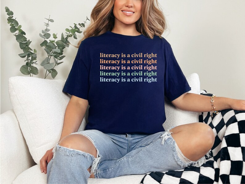 May include: A navy blue t-shirt with the text "literacy is a civil right" repeated five times in a gradient of pink, orange, and green.