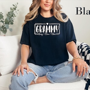 May include: A black short-sleeved t-shirt featuring white text that reads GRAMMY inside a rectangular frame with a small heart above it. Below the frame, the names Daisy, Elena, and Chris are printed, each separated by a small heart.