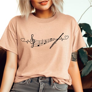 Może przedstawiać: Jasnor&oacute;żowy t-shirt z czarnym nadrukiem przedstawiającym nutę muzyczną, flet i bicie serca.