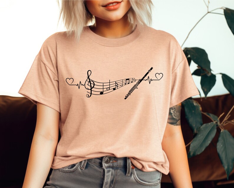 Może przedstawiać: Jasnor&oacute;żowy t-shirt z czarnym nadrukiem przedstawiającym nutę muzyczną, flet i bicie serca.