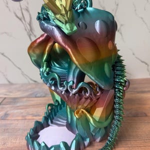 May include: A multi-colored dragon figurine with a crown and a spiky tail. The dragon is in shades of blue, green, yellow, and red. The base of the figurine has a geometric design. The figurine has the text "AUTHORIZED SELLER" on the top left.