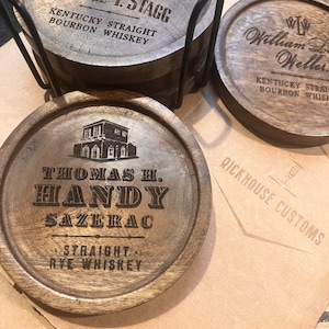 May include: Four wooden coasters with different bourbon brands engraved on them. The coasters are stacked on top of each other and have a metal ring holding them together. The brands are George T. Stagg Kentucky Straight Bourbon Whiskey, William L. Weller Kentucky Straight Bourbon Whiskey, Thomas H. Handy Sazerac Straight Rye Whiskey, and Rickhouse Customs.