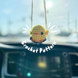 May include: A yellow crocheted chick on a swing hanging from a rearview mirror in a car. The text "Crochet Pattern" is written below the chick.