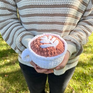 May include: A crocheted coffee cup with a white rim and a pink interior. The cup has a leaf design on the top.