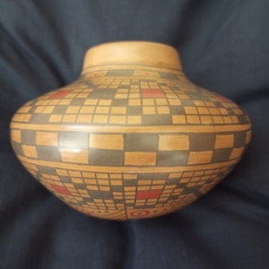 Op de afbeelding: Een bruine keramische pot met een geometrisch ontwerp in zwart en rood. De pot heeft een ronde vorm en een brede opening.