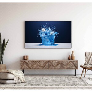 Peut inclure: Une éclaboussure de peinture bleue avec des fleurs blanches sur un fond bleu foncé. L'éclaboussure coule le long du côté de la toile. L'image est encadrée et accrochée à un mur blanc au-dessus d'une console en bois.