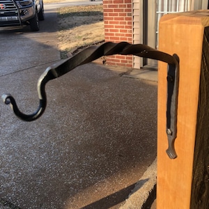 Peut inclure: Un crochet en métal noir avec un design torsadé est monté sur un poteau en bois. Le crochet est incurvé à l'extrémité et présente un détail décoratif à la base.