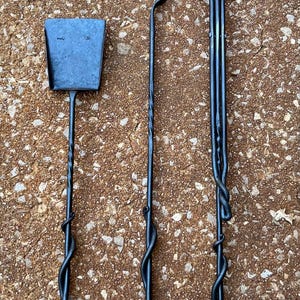 May include: A set of three black wrought iron fireplace tools including a shovel, a poker with a hooked end, and a three-pronged fork. Each tool features a long, slender handle with a decorative twisted metal design near the base.