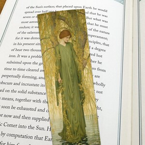 May include: A bookmark featuring a painting of a woman in a green dress standing in a forest. The woman is looking down at the ground. The background is a lush green forest with a stream of water.