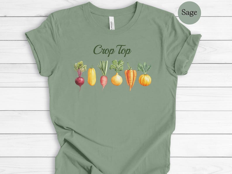 May include: Sage green crop top t-shirt with the words "Crop Top" in a script font. Below the text is a watercolor illustration of various vegetables, including a beet, squash, carrot, onion, and pepper.