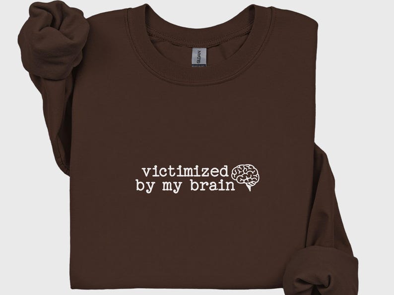 May include: A dark brown sweatshirt with the phrase "victimized by my brain" printed in white, accompanied by a white brain graphic. The sweatshirt has a crew neck and long sleeves.