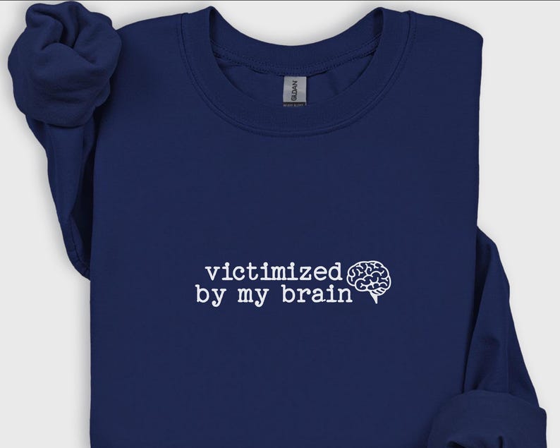 May include: A navy blue sweatshirt with the phrase "victimized by my brain" in white text, accompanied by a brain graphic. The sweatshirt is made of a soft material and has a crew neck.