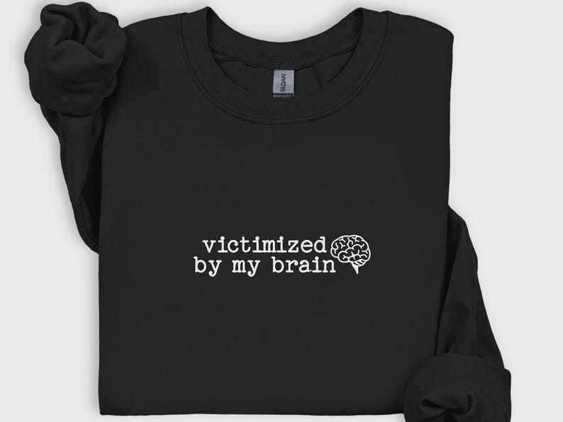 May include: Black sweatshirt with the text "victimized by my brain" in white, accompanied by a white brain graphic. The sweatshirt is made of a soft material and has a crew neck.