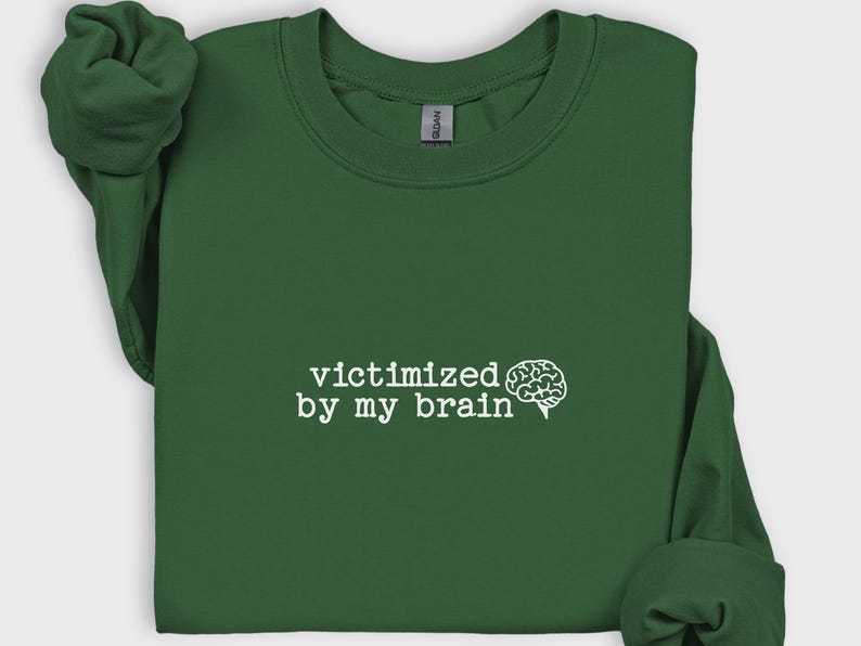 May include: A dark green sweatshirt with the phrase "victimized by my brain" in white text, accompanied by a white brain graphic. The sweatshirt has long sleeves and a crew neck.