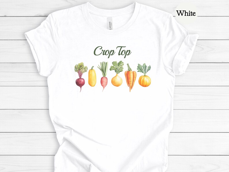 May include: White crop top t-shirt with a watercolor illustration of various vegetables, including a beet, zucchini, carrot, turnip, pepper, and pumpkin. The words "Crop Top" are printed in green cursive above the vegetables.