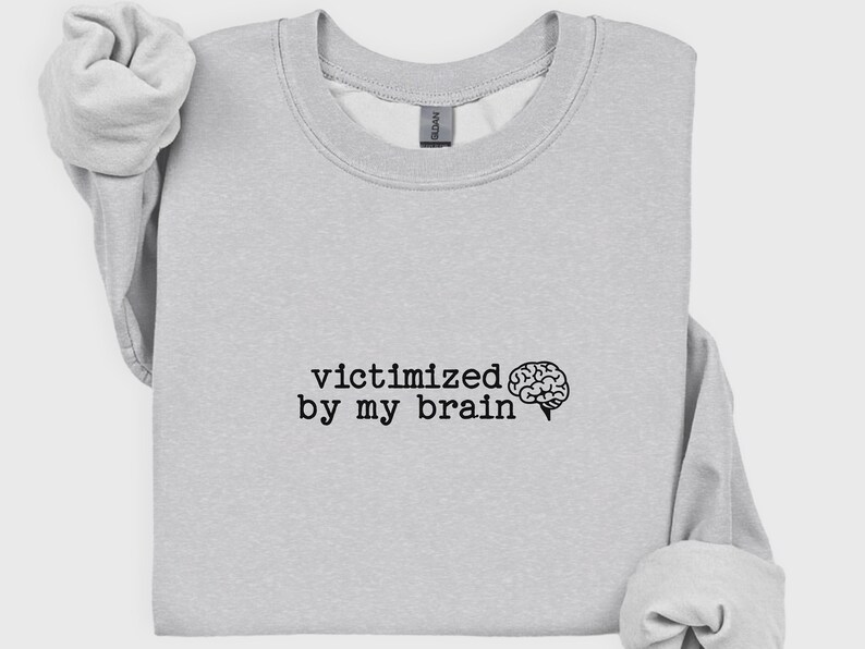May include: Light gray sweatshirt with the phrase "victimized by my brain" in black text, accompanied by a brain graphic. The sweatshirt has a crew neck and long sleeves.