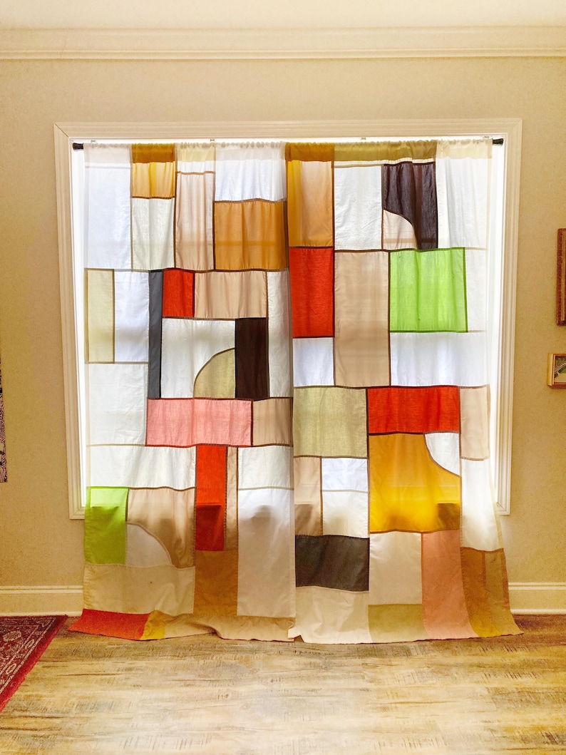 May include: A pair of curtains featuring a patchwork design composed of rectangular and square fabric panels in various colors including white, orange, yellow, lime green, brown, and tan, hanging from a rod over a window frame.