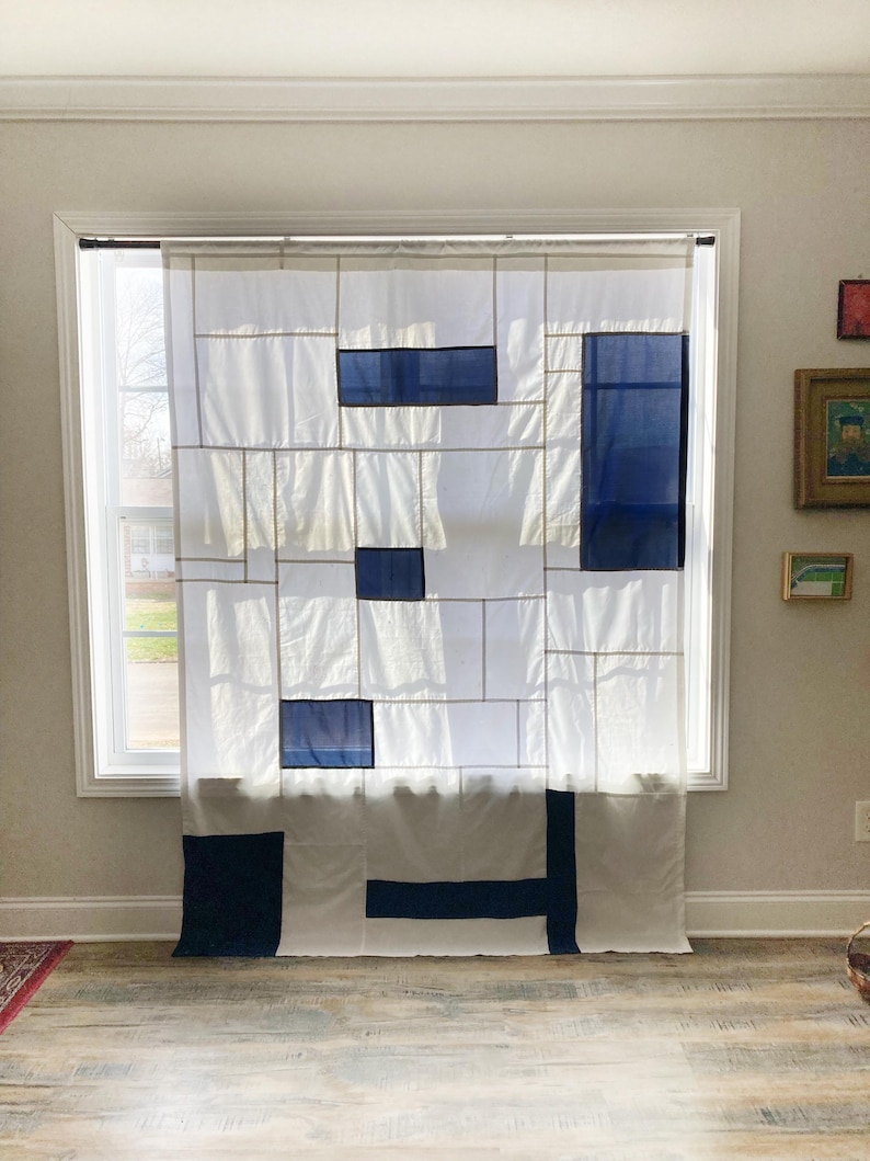 May include: A white curtain featuring a geometric grid pattern with rectangular navy blue fabric panels. The design consists of thin vertical and horizontal lines intersecting to create various rectangular sections across the semi-sheer fabric.