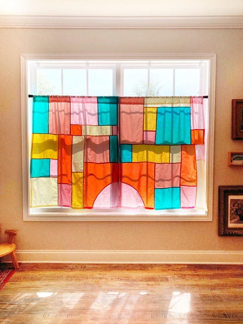 May include: A pair of window curtains featuring a patchwork design of translucent fabric panels in vibrant shades of turquoise, yellow, orange, pink, and red. The rectangular and arched segments are stitched together, allowing light to filter through.