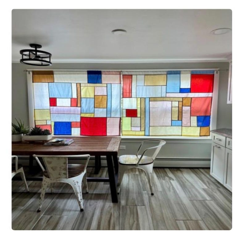 May include: A pair of window curtains featuring a grid of rectangular panels in primary colors including red, blue, and yellow, interspersed with white and light-toned sections. The fabric is semi-translucent, allowing light to pass through the pattern.