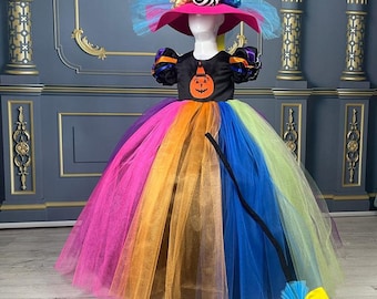 May include: A rainbow tulle dress with a black bodice featuring a pumpkin design. The dress is paired with a pink witch hat with black and white striped accents and a yellow and blue broom.