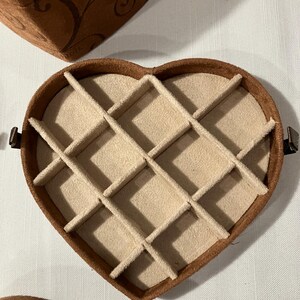 May include: A heart-shaped jewelry box with a brown exterior and a beige interior divided into compartments. The box is open, revealing the interior design. Another box is partially visible in the background.