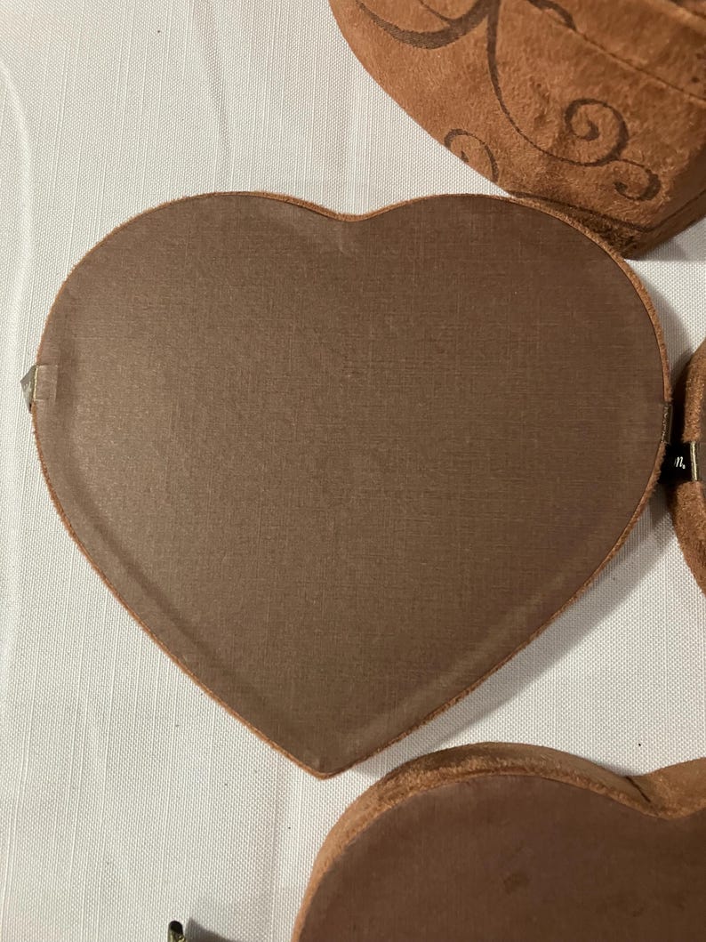 May include: Several heart-shaped boxes in varying sizes. The boxes are a warm brown color with a textured surface. Some boxes have decorative swirl patterns. The boxes are arranged on a white surface.