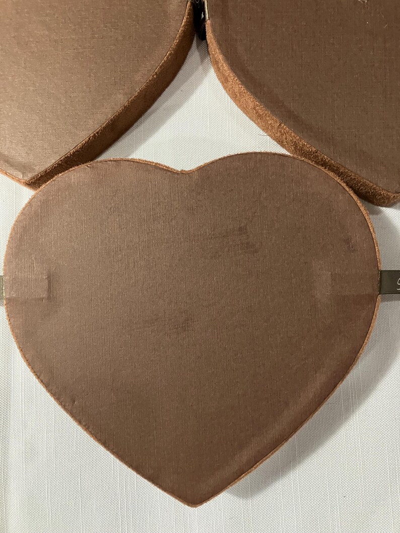 May include: Close-up of several heart-shaped boxes in a warm brown color. The boxes have a textured surface and a darker brown trim. The boxes are arranged on a white surface.