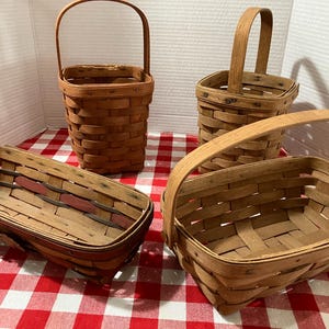 May include: A collection of four woven wooden baskets featuring natural brown tones. Two baskets are tall with upright handles, while the other two are rectangular with low-profile handles. The construction shows visible overlapping wood strips.