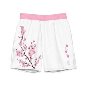 May include: White athletic shorts with a pink waistband and a pink cherry blossom print on the left leg. The right leg has a small pink floral design and a logo.