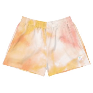 May include: Tie-dye shorts in shades of yellow, orange, and pink. The shorts have a white elastic waistband and a small logo on the right side.