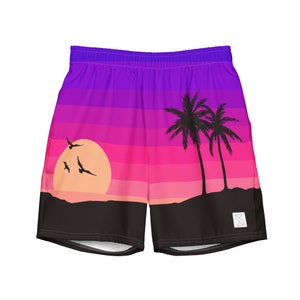 May include: Shorts featuring a vibrant sunset design with shades of purple, pink, and orange. The graphic includes a sun, palm trees, and flying birds. The shorts have an elastic waistband and a small logo on the right leg.