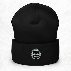 May include: Black beanie with a white embroidered cartoon face with green hair and headphones.