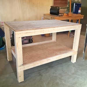 May include: A simple, wooden workbench with a single shelf. The workbench is made of unfinished plywood and has a natural wood finish.
