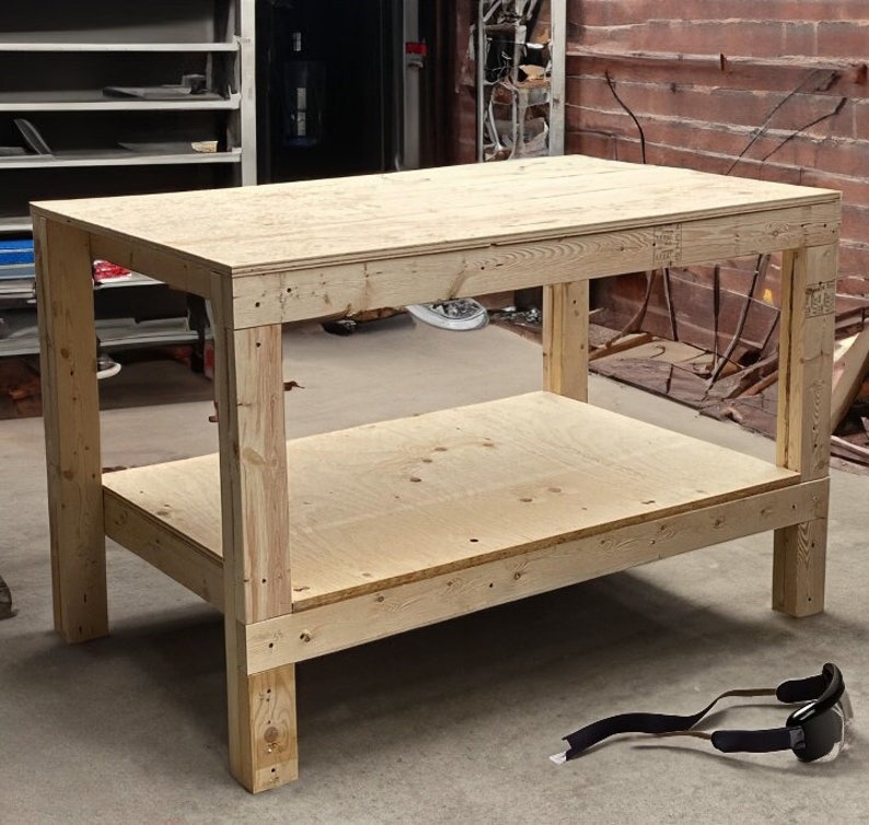 May include: A wooden workbench with a top shelf and a lower shelf. The workbench is made of unfinished plywood and has a natural wood color.