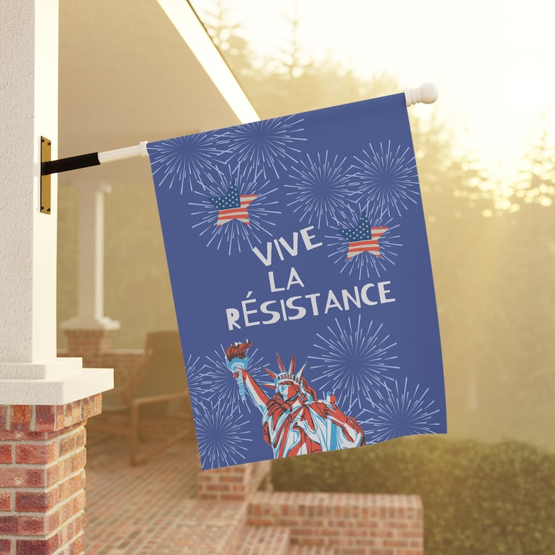 Peut inclure: Un drapeau bleu avec le texte "VIVE LA R&Eacute;SISTANCE" et des illustrations de feux d'artifice, de la Statue de la Libert&eacute; et de drapeaux am&eacute;ricains. Le drapeau est accroch&eacute; &agrave; l'ext&eacute;rieur sur un poteau blanc.