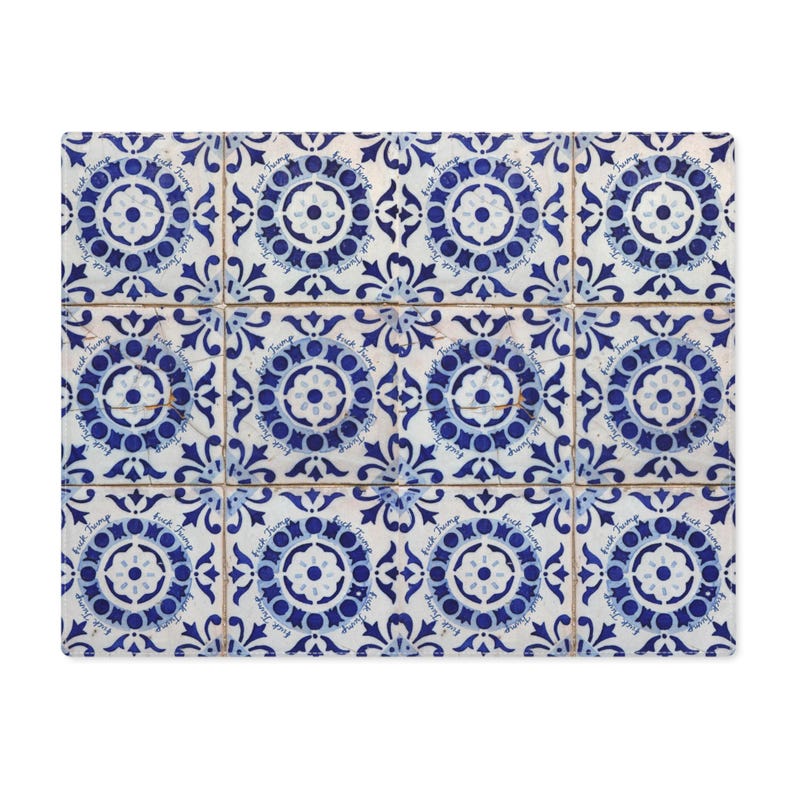 Pu&ograve; includere: Cuscino rettangolare con un motivo ripetuto di piastrelle blu e bianche. Ogni piastrella presenta un motivo floreale e il testo "fuck trump". Il design del cuscino ricorda le piastrelle tradizionali.