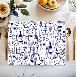 May include: White placemat with a blue wine and food pattern. The design includes wine bottles, glasses, cheese, grapes, and lemons. The text "Fuck Trump" is visible on some bottles. Gold silverware and a white table setting are in the background.