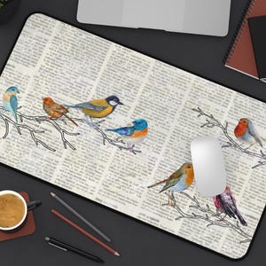 Puede incluir: Una alfombrilla de ratón blanca con un fondo de impresión de periódico y pájaros coloridos posados ​​en ramas. Los pájaros son azules, amarillos, naranjas y rojos.