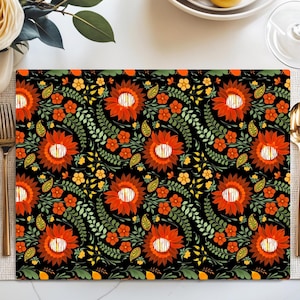 Puede incluir: Un mantel individual rectangular con un fondo negro y un vibrante estampado floral. El diseño presenta grandes flores naranjas con centros blancos, rodeadas de flores más pequeñas naranjas y amarillas, hojas y tallos verdes. Cubiertos dorados a la izquierda y a la derecha.