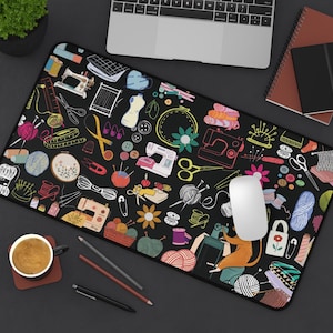 May include: Black rectangular mousepad with a colorful sewing and crafting design. The pattern includes sewing machines, scissors, yarn, needles, and other craft-related illustrations. A white computer mouse sits on the pad, near a laptop.