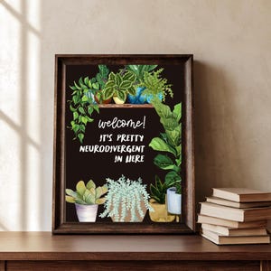 May include: A framed wall art print with a black background featuring various potted plants and the white text: welcome! IT'S PRETTY NEURODIVERGENT IN HERE. The illustration includes green foliage, succulents, and trailing vines in colorful pots.