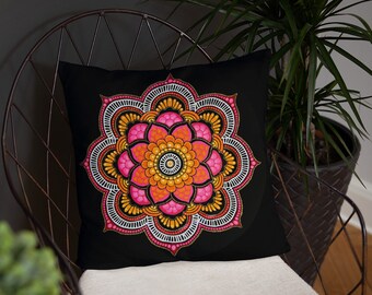 May include: A black pillow with a pink, orange, and gold mandala design. The mandala is intricate and detailed, with a circular pattern of dots and lines.
